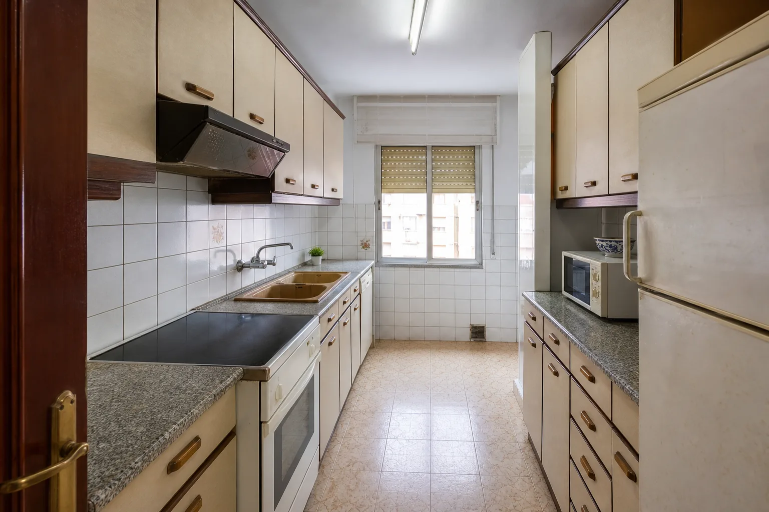 Cocina antigua en paralelo con muebles crema, encimera gris y suelo estampado
