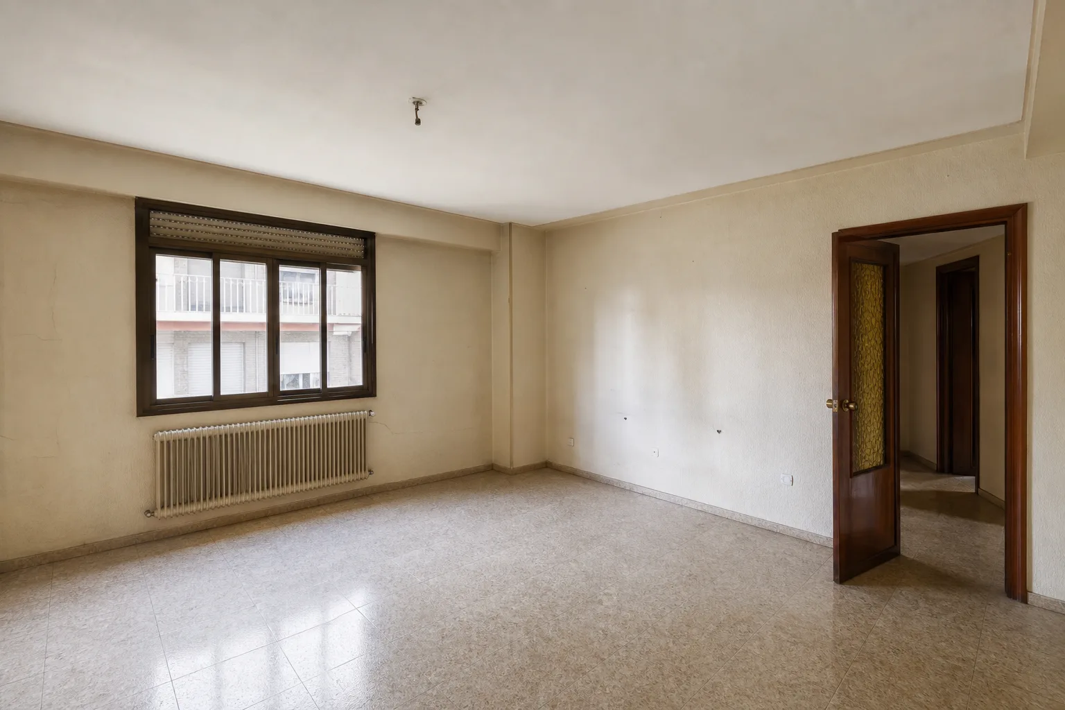 Salón antiguo con suelo cerámico, paredes crema y carpintería oscura