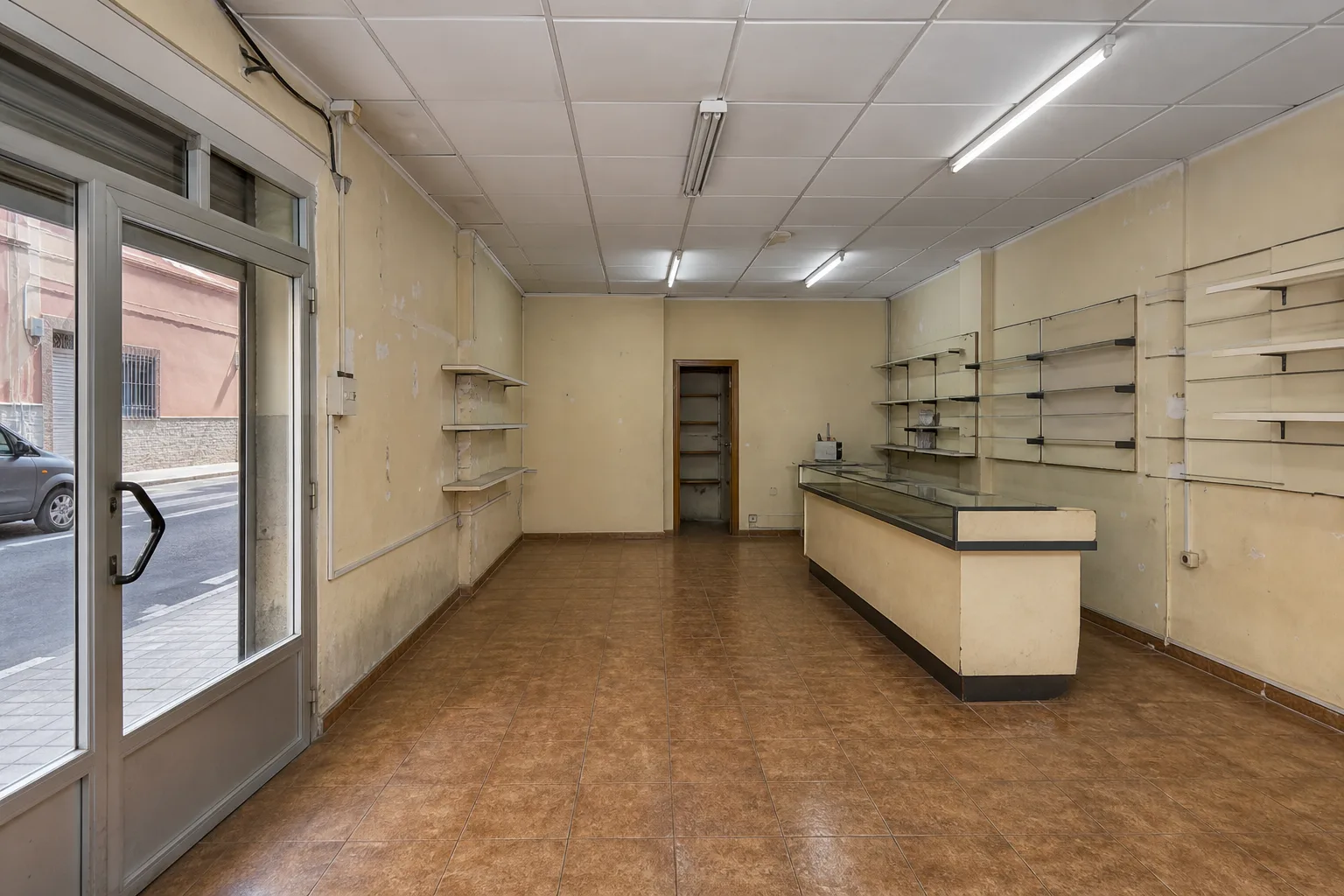 Local comercial antiguo con suelo marrón, fluorescentes y estanterías vacías