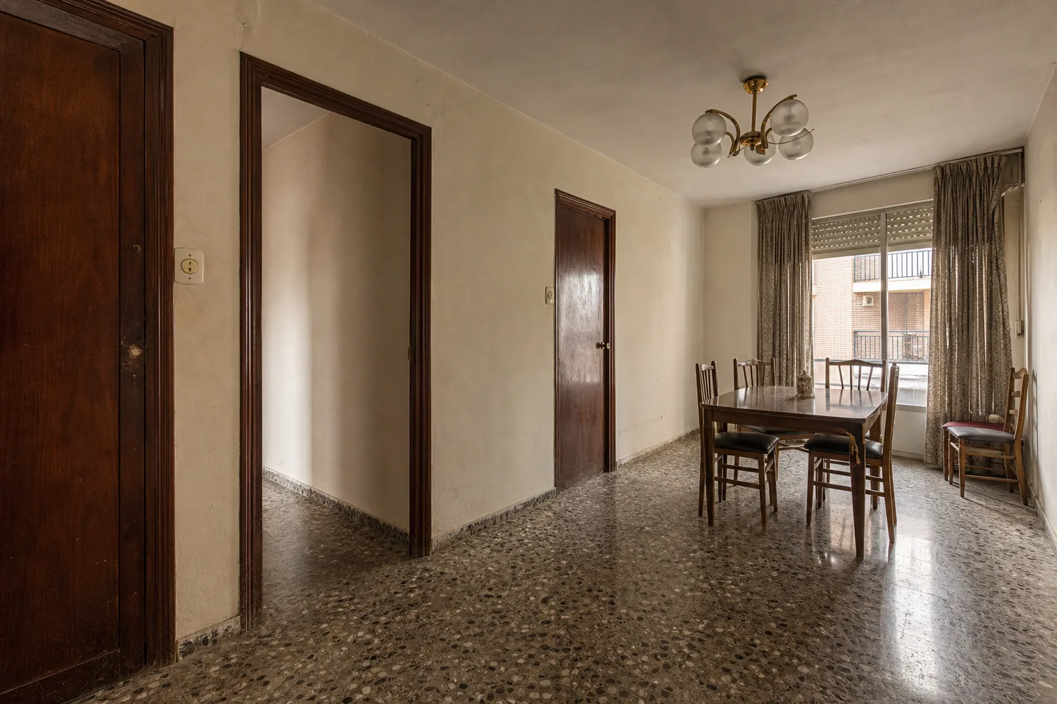 Comedor de piso antiguo con terrazo, puertas oscuras y paredes envejecidas